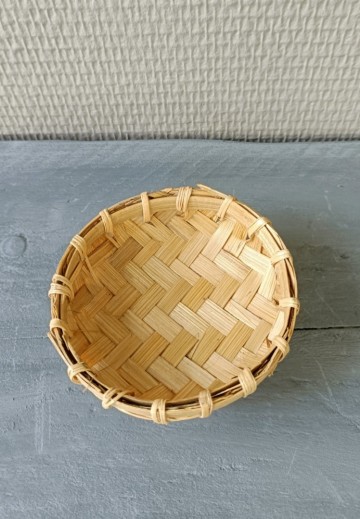 Bovenaanzicht van een leeg, gevlochten bamboe offerschaaltje van 8 cm op een grijze houten ondergrond