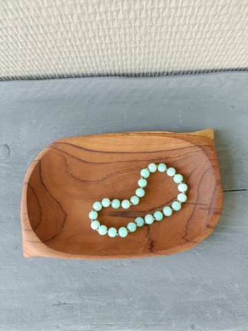 Een handgemaakt teakhouten sieradenschaaltje gebruikt als opbergvakje met een mintgroene kralenarmband erin